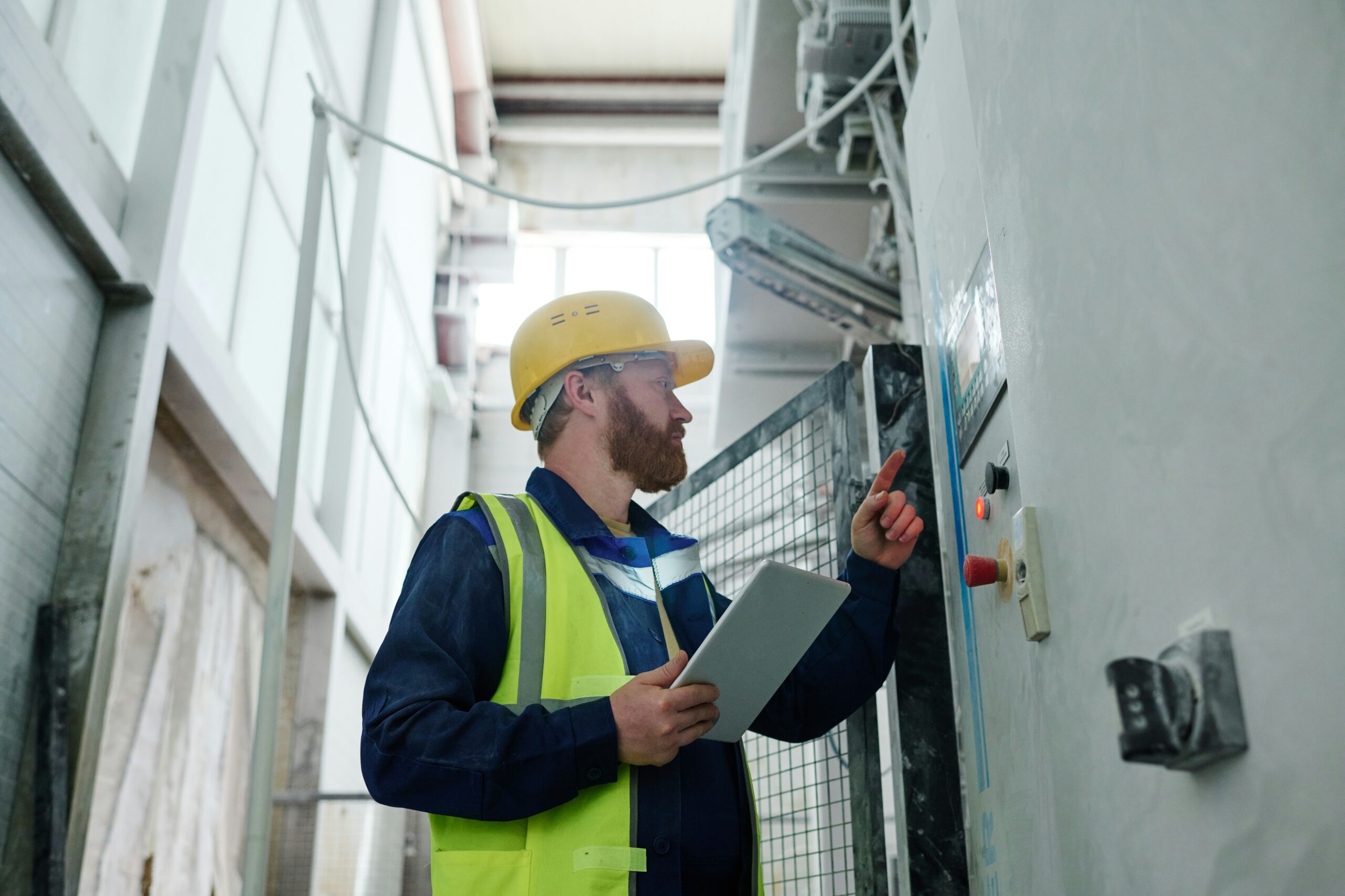 Técnico com capacete e óculos de segurança inspecionando painel de comando industrial para laudo elétrico NR-10